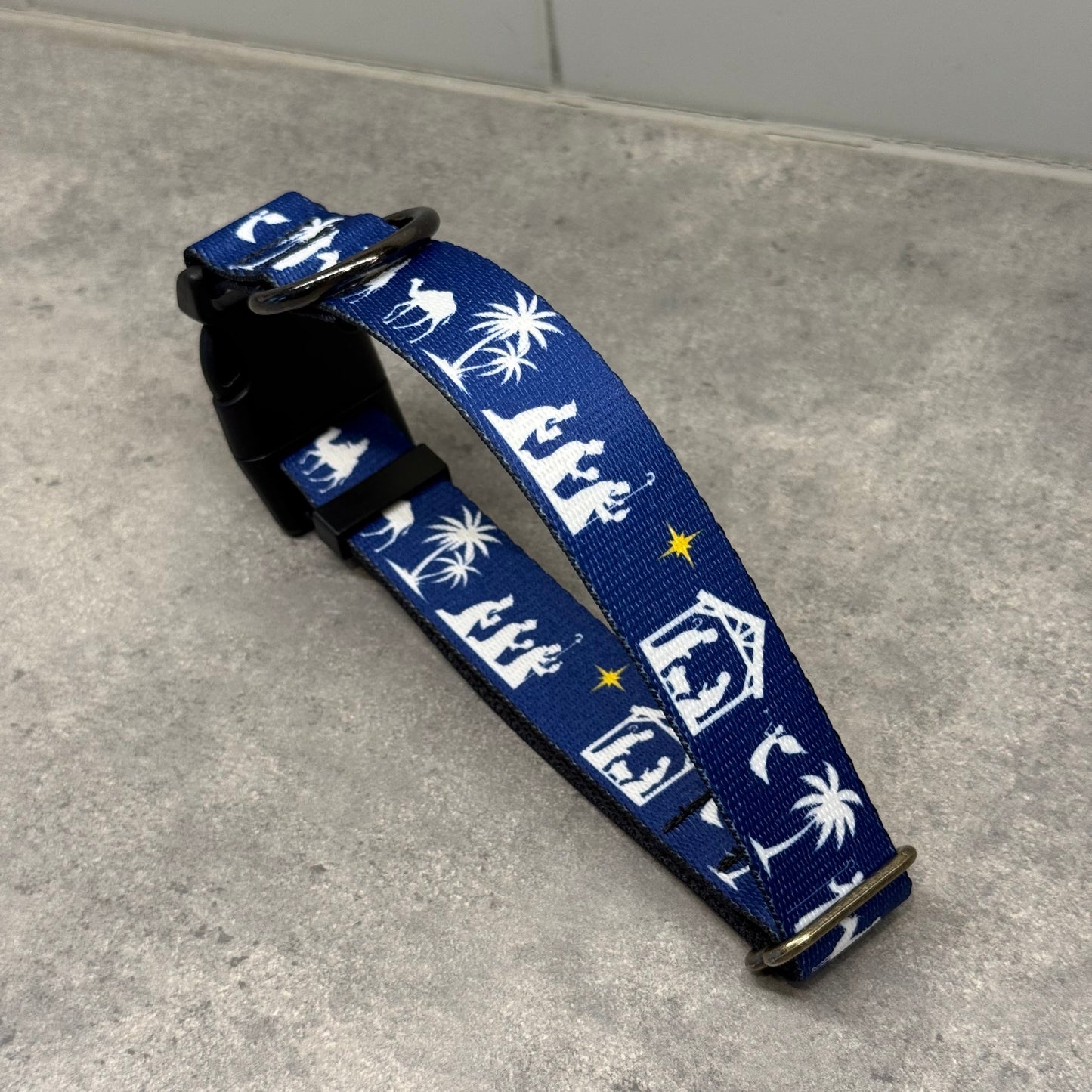 Blue dog collar with white nativity scene design on a gray floor.